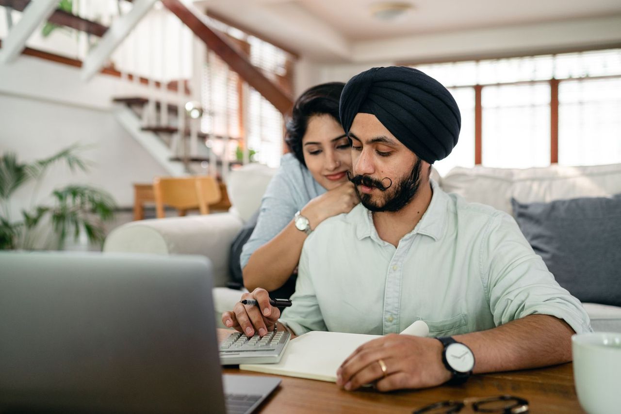 A couple sitting together at their kitchen table with a laptop and calculator, smiling as they plan