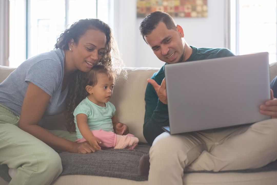 A young family on their sofa, looking at a laptop together and smiling