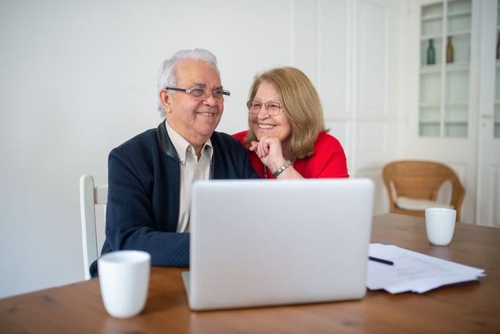 An older couple sitting together at a table, smiling as they look at a laptop