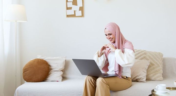 A woman on her sofa at home, smiling during a video call with her laptop